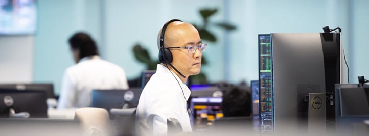 Ansatt ved Singapore-kontoret arbeider foran skjerm med markedsdata, iført hodesett i et åpent kontorlandskap.
