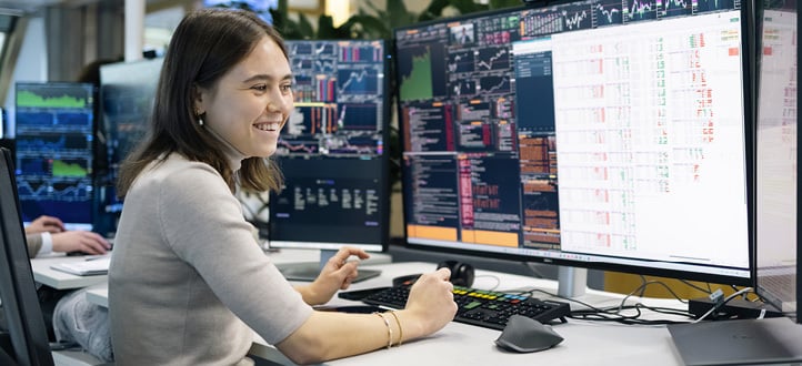 Ansatt ved Oslo-kontoret arbeider foran flere skjermer med markedsdata og analyser i et åpent kontorlandskap.