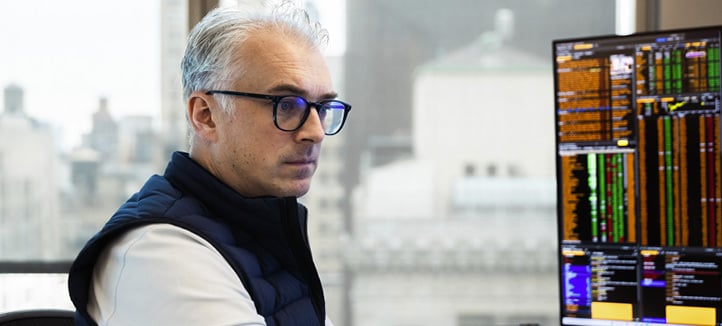 Ansatt ved New York-kontoret arbeider foran skjerm med markedsdata, med utsikt over bylandskapet i bakgrunnen.
