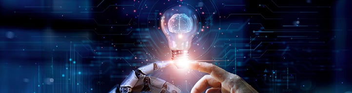 Human and robotic hands touching beneath a glowing light bulb, symbolising innovation and technology.