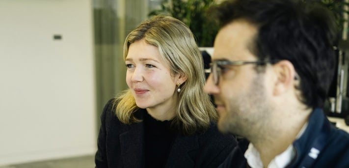 To ansatte i samtale ved et skrivebord i et kontor.