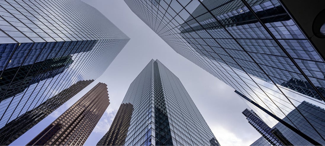 Utsikt opp mot moderne glasskledde skyskrapere i en by.