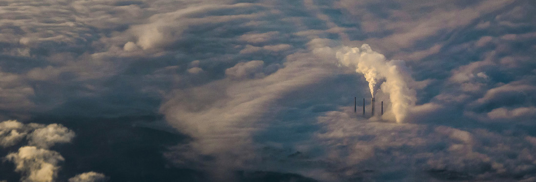 Luftfoto av fabrikkpiper med røyk over skydekke.